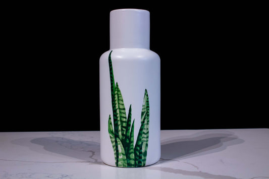 Jarrón florero de cerámica forma cilíndrica con la parte de arriba más angosta color blanco con diseño en hojas alargadas en verde