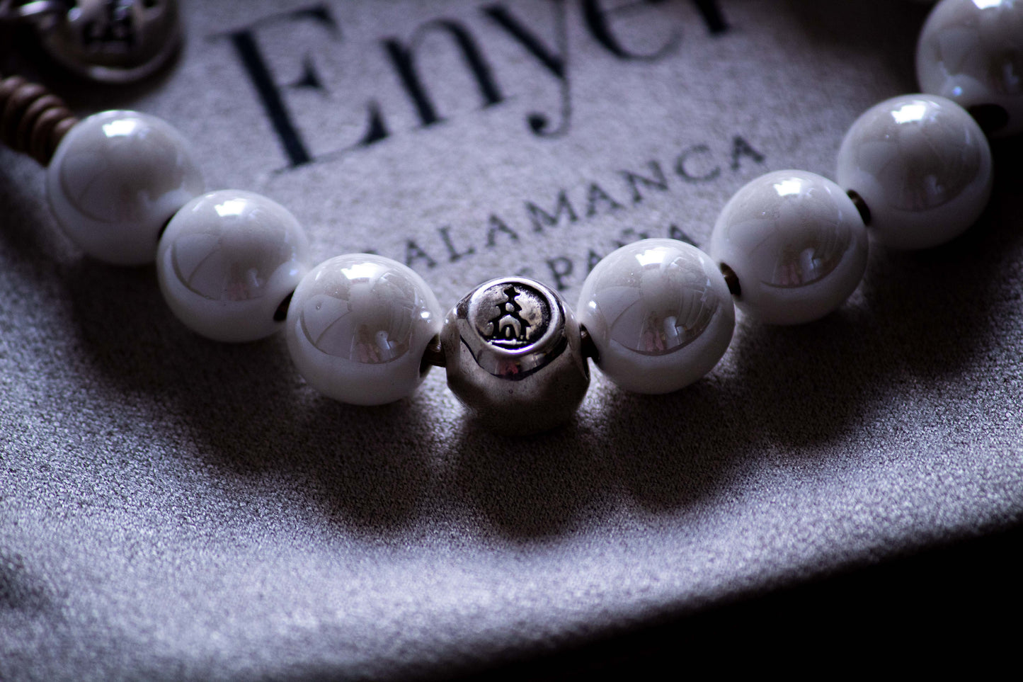 Detalle de Pulsera Denario con esferas blancas brillantes y esfera en plata con relieve de simbología religiosa