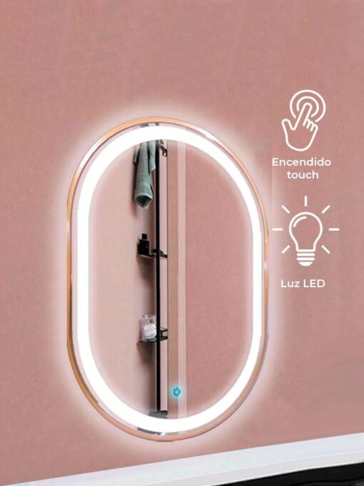 Espejo ovalado en vertical contorno interior iluminado y el exterior en dorado reflejando unos accesorios de baño, con símbolos de "encendido touch" y "luz led"