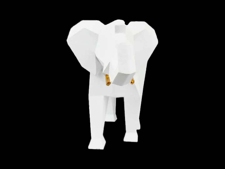 Figura decorativa blanca en forma de elefante con contornos remarcados con apariencia geométrica y colmillos dorados en posición frontal