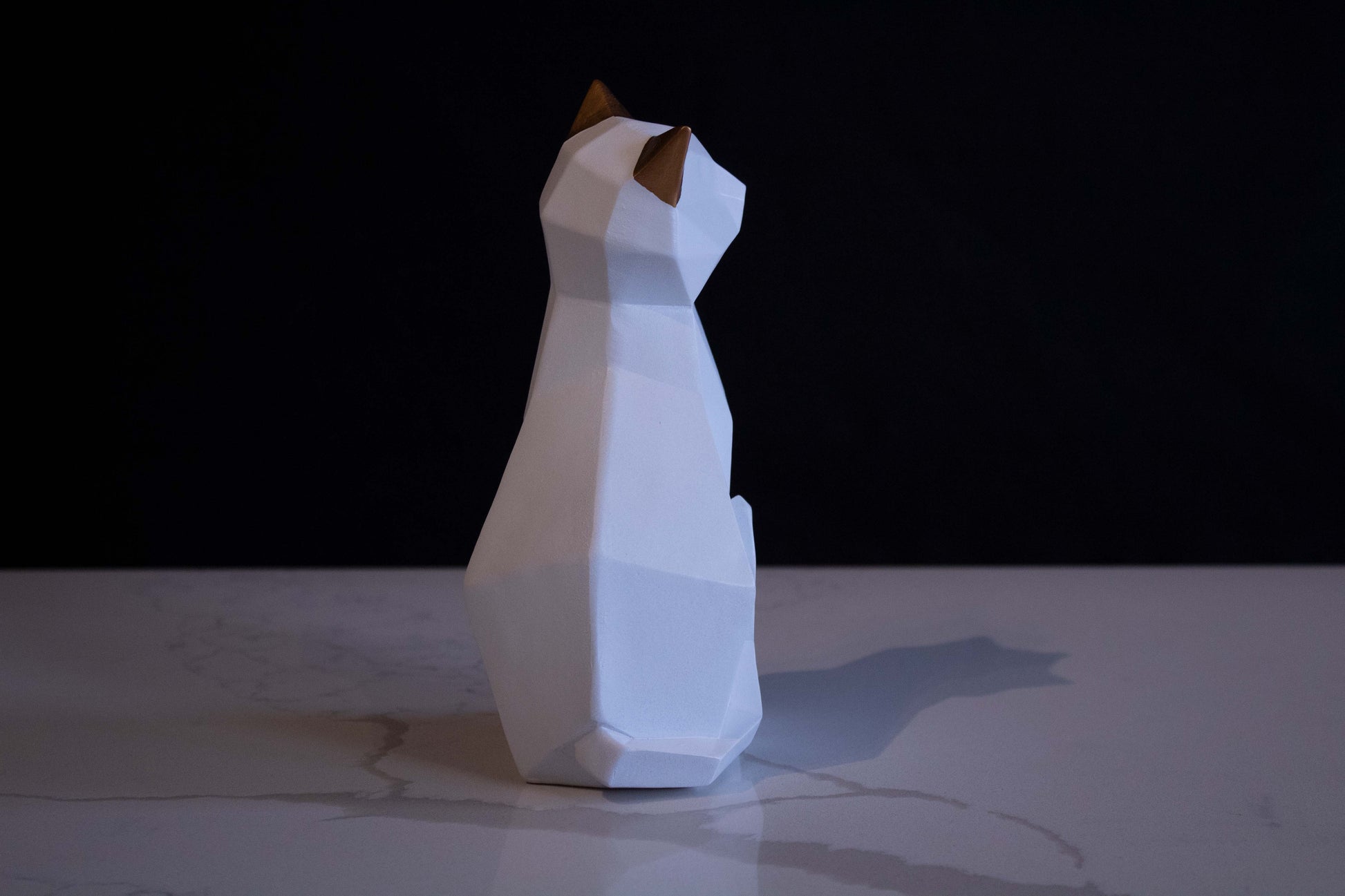 Figura de ornato en forma de gato blanco sentado con orejas doradas vista por atrás con contorno en líneas marcadas