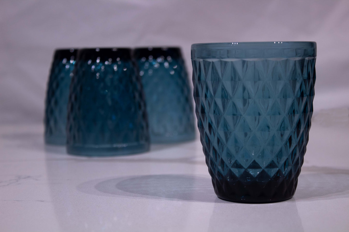 Cuatro vasos de cristal azul con diseño de diamante uno al frente y tres atrás boca abajo