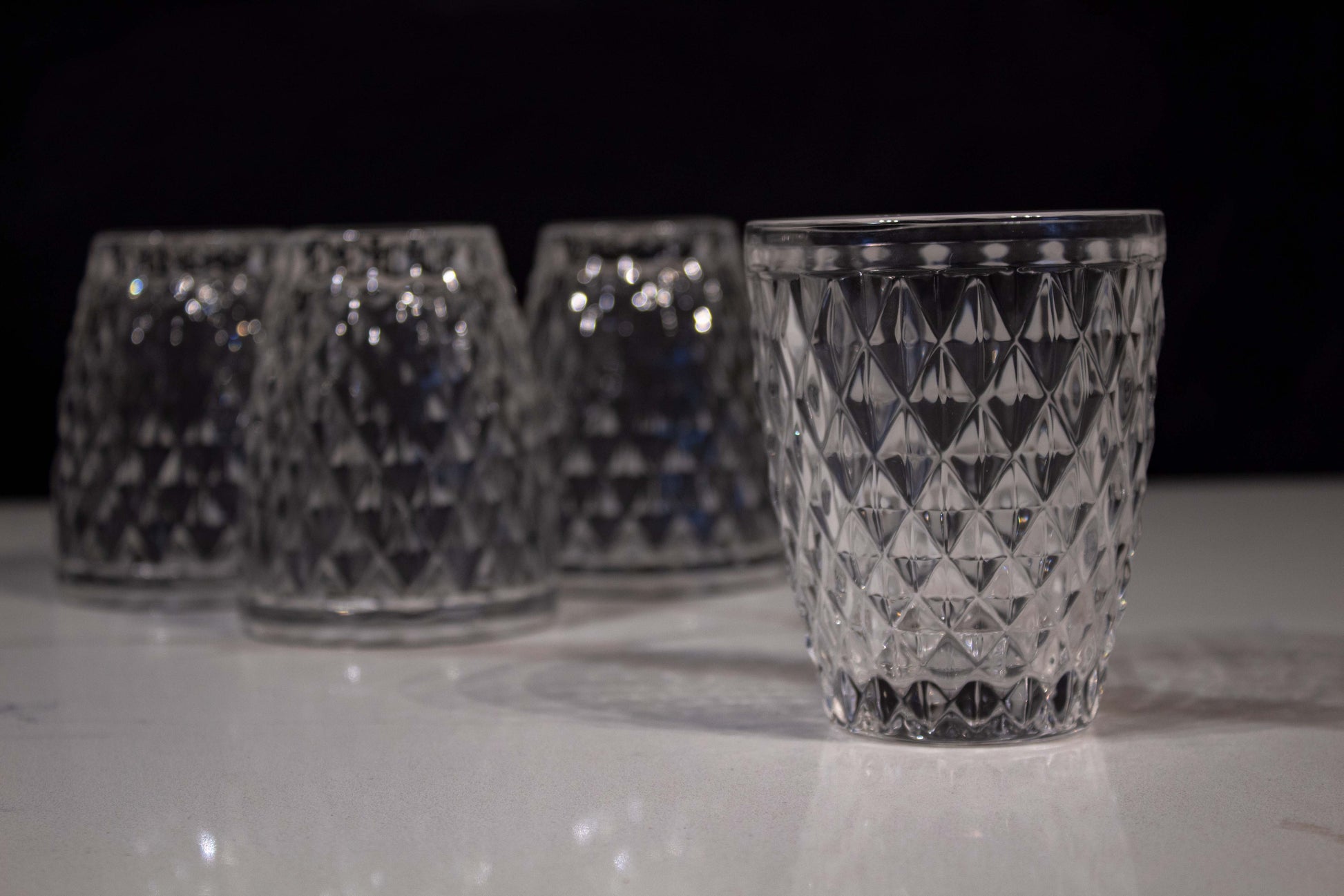 Cuatro vasos de cristal transparente con diseño de diamante uno al frente y tres atrás boca abajo