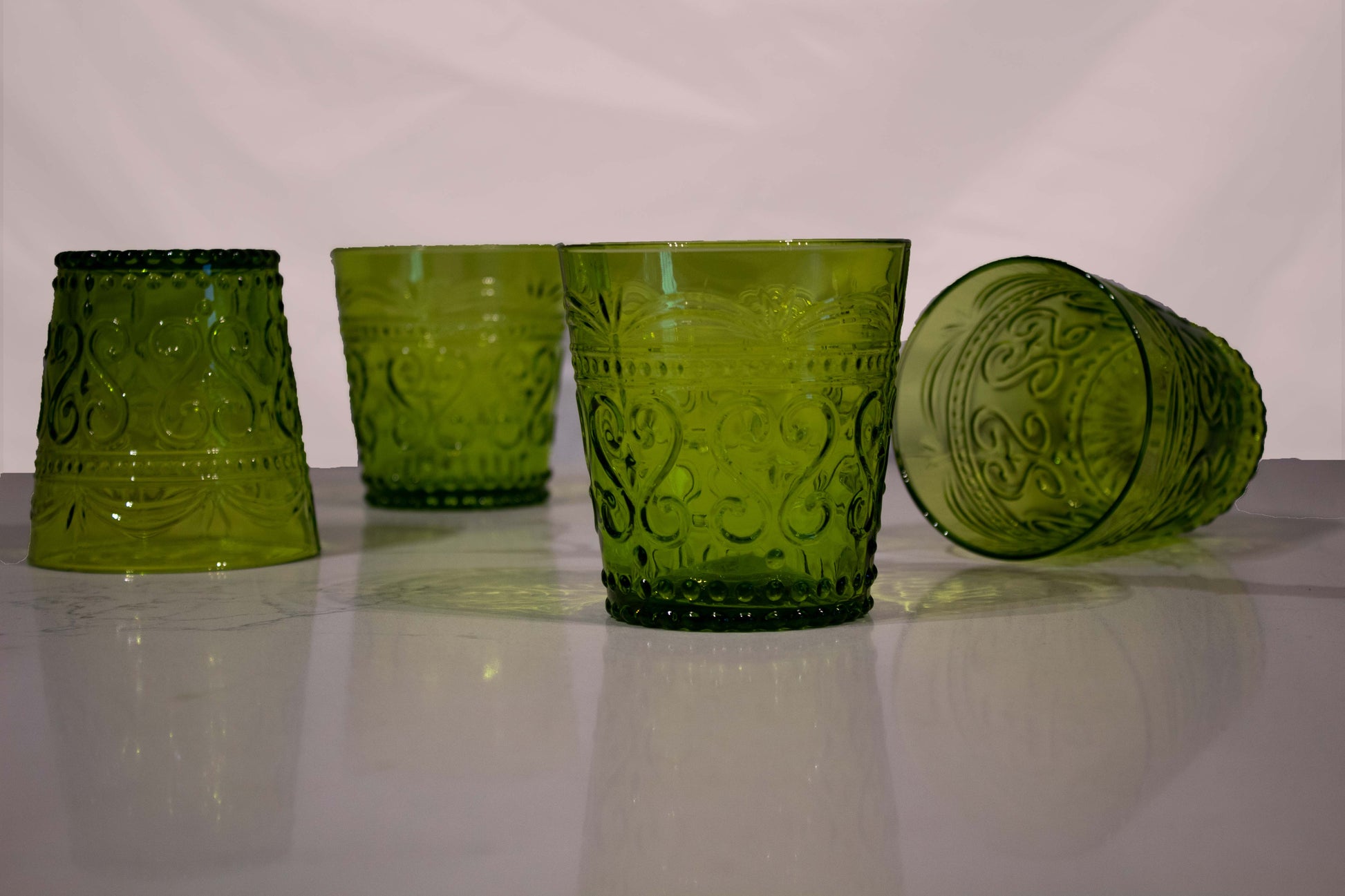 Cuatro vasos de cristal verde con diseño de grecas y estilo de vidrio soplado, uno de ellos tirado