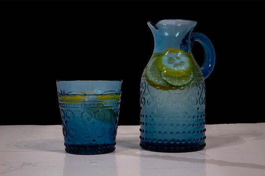 Vaso y jarra de cristal azul con diseño de grecas y estilo de vidrio soplado llenos de agua con rodajas de limón