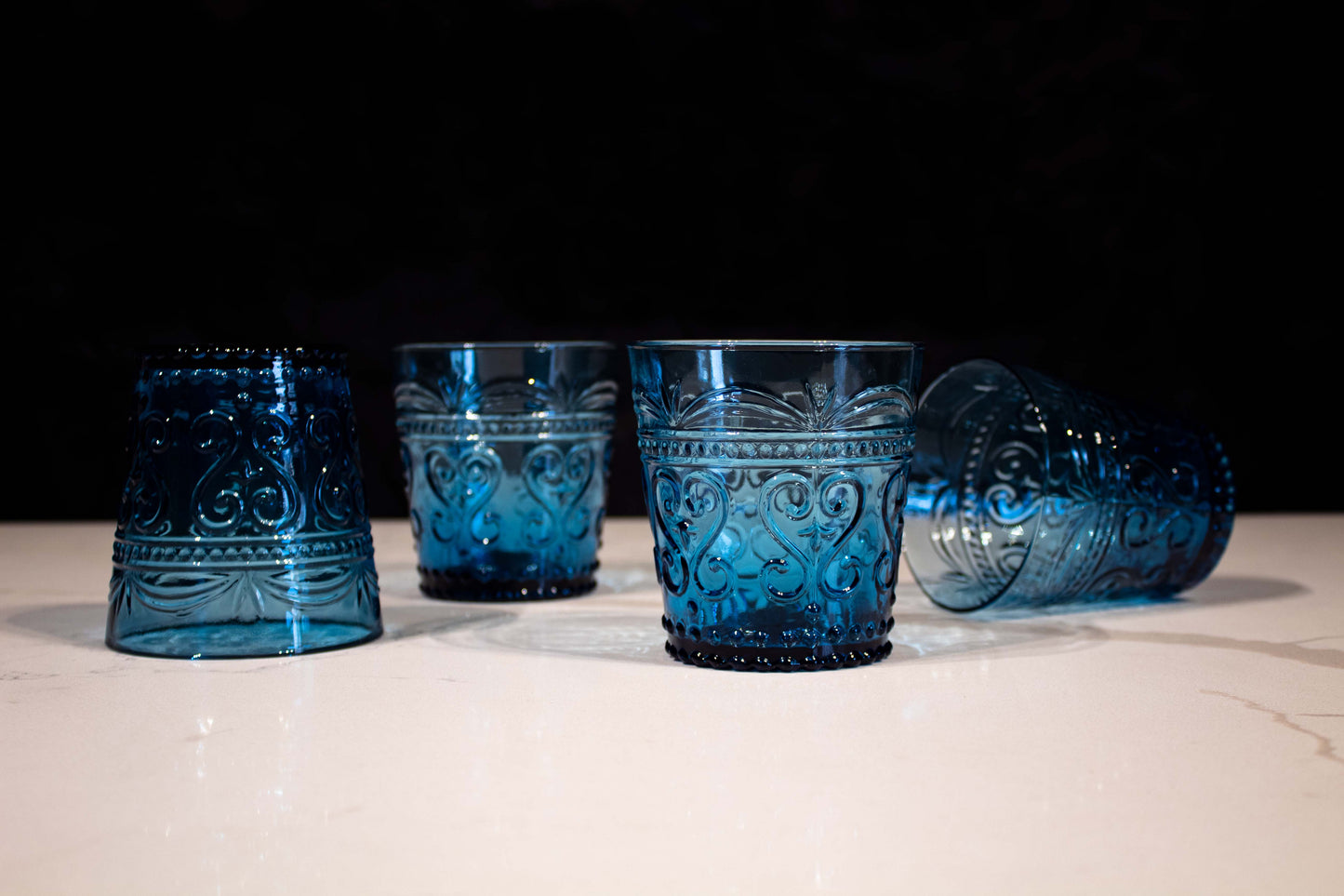 Cuatro vasos de cristal azul con diseño de grecas y estilo de vidrio soplado, uno de ellos tirado